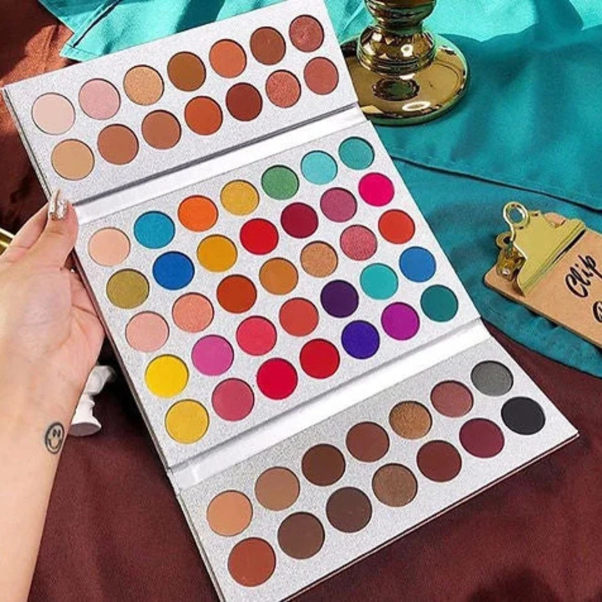 Makeup palette with a variety of colors held by a hand on a colorful background